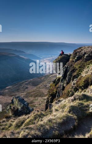 Walker seduto su Laddow Rocks, affacciato sulla valle di Crowden Great Brook, sul Peak District National Park, Derbyshire, Inghilterra, Regno Unito, Europa Foto Stock