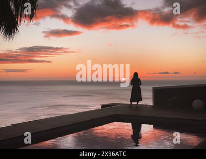 Silhouette di una giovane donna che si affaccia sull'oceano Atlantico al tramonto con riflessi nella piscina privata, paradiso tropicale estivo, Orange pi Foto Stock