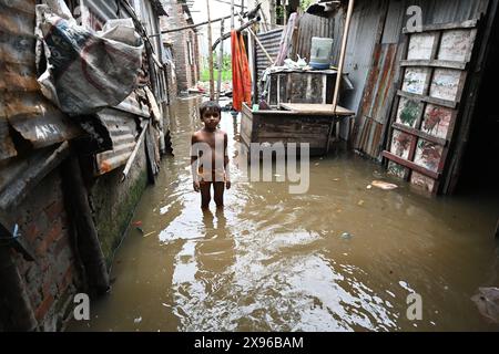 Un bambino di baraccopoli dorme attraverso un cortile allagato a seguito di forti piogge dopo l'atterraggio del ciclone Remal nella baraccopoli di Balumath a Dacca, Bangladesh, il 29 maggio 2024 Foto Stock