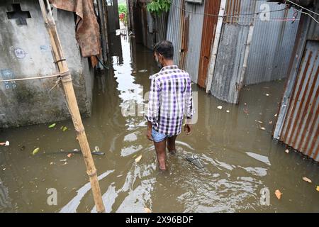 Un popolo di baraccopoli cammina attraverso un cortile allagato a seguito di forti piogge dopo l'atterraggio del ciclone Remal nella baraccopoli di Balumath a Dacca, Bangladesh, il 29 maggio 2024 Foto Stock