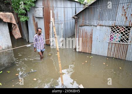 Un popolo di baraccopoli cammina attraverso un cortile allagato a seguito di forti piogge dopo l'atterraggio del ciclone Remal nella baraccopoli di Balumath a Dacca, Bangladesh, il 29 maggio 2024 Foto Stock