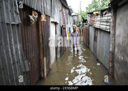 Un popolo di baraccopoli cammina attraverso un cortile allagato a seguito di forti piogge dopo l'atterraggio del ciclone Remal nella baraccopoli di Balumath a Dacca, Bangladesh, il 29 maggio 2024 Foto Stock