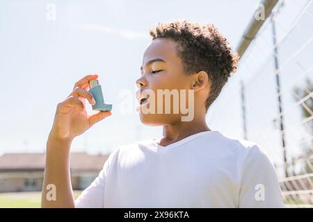 Il bambino sta usando un inalatore per asma nel parco Foto Stock