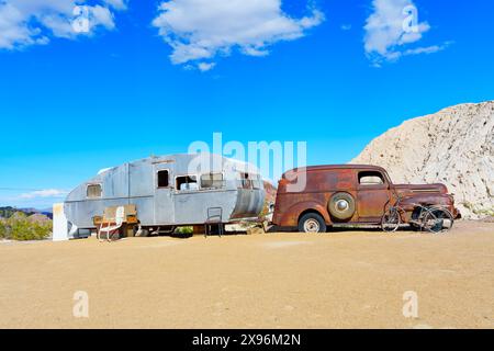 Nelson, Nevada - 15 aprile 2024: Auto d'epoca pesantemente arrugginita attaccata a una carovana invecchiata e maltempo ambientata in un ambiente desertico Foto Stock