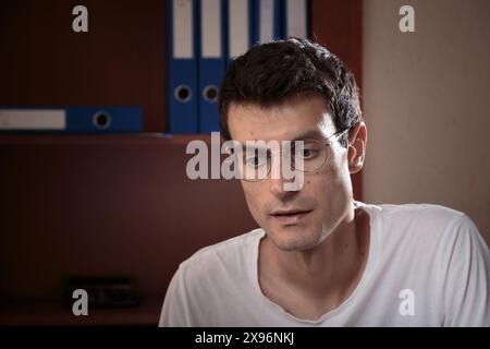 Ritratto di un giovane concentrato. La foto è stata scattata in ufficio e ci sono delle cartelle sullo sfondo. Primo piano. Foto Stock