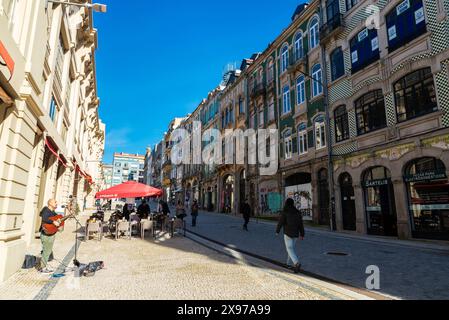 Oporto, Portogallo - 23 novembre 2023: Chitarrista di strada musicista in una strada commerciale con negozi, ristoranti e gente intorno a Porto o Oporto, Por Foto Stock