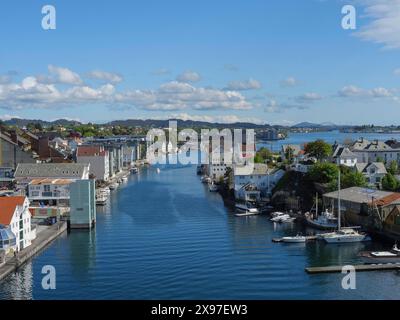 Un pittoresco corso d'acqua in una città circondata da edifici e barche sotto un cielo blu con nuvole, porto in norvegia con barche, navi e molte case Foto Stock