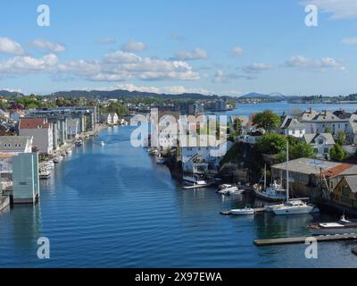 Un bellissimo canale in una città circondata da edifici e barche sotto un cielo limpido con nuvole, porto in norvegia con barche, navi e molte case Foto Stock