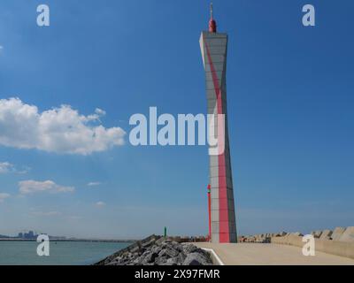 Un faro rosso e bianco si erge accanto a una strada sul mare sotto un cielo nuvoloso, fari ad un ingresso del porto sul mare in Belgio contro a Foto Stock