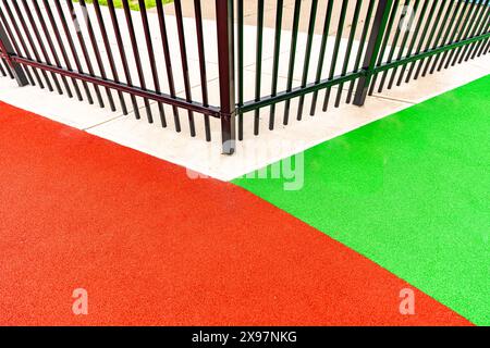 Foto ravvicinata di una recinzione ornamentale in metallo nero che circonda una superficie di gioco multicolore. Foto Stock