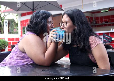 Due giovani donne latine bruna di 20 anni bevono cocktail blu ghiacciato con peperoncino, festeggiano bevendo alcolici Foto Stock