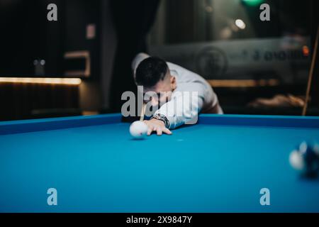 Giovane concentrato che gioca a biliardo in una sala da biliardo poco illuminata Foto Stock