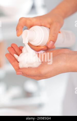 Mani estetiste che trattengono il flacone bianco con schiuma pelante o detergente. Estetista esperto che si prepara ad applicare schiuma detergente in un centro di bellezza. Pelle viso idratante, massaggio viso. Foto Stock