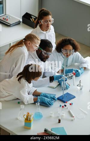 Vista verticale ad angolo alto di giovani insegnanti afroamericani e gruppo di studenti delle scuole medie che fanno esperimenti durante la classe di chimica Foto Stock