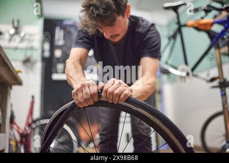 Riparatore di biciclette ispanico che monta uno pneumatico senza aria su una ruota da bici presso la sua officina di riparazione. Composizione selettiva della messa a fuoco con spazio di copia. Foto Stock