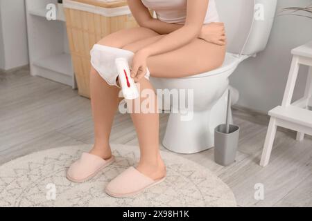 Giovane donna con imbottitura mestruale seduta sulla ciotola del bagno in bagno Foto Stock