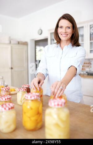 Donna matura, ritratto e felice, pesche conservate in salute e conservazione del cibo in cucina. Nutrizionista, economia domestica per il raccolto e la pulizia Foto Stock