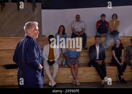 Docente femminile di abbigliamento formale sorridente, tenendo conferenze a gruppi di persone sullo sfondo, le persone si sono riunite per ascoltarla parlare di me Foto Stock