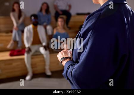 Foto ravvicinata di mani di oratrice donna corta in abbigliamento formale in piedi nella sala conferenze, gruppo di diverse persone interrazziali sedute nel backgrou Foto Stock
