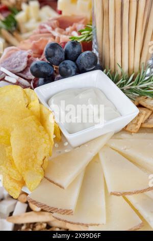 Tagliere di salumi parte di tapas in stile spagnolo o aperitivo con fette di formaggio Manchego a forma di ventaglio, patatine fritte, piccolo piatto di salsa Foto Stock