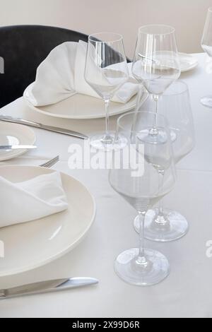 Tavolo da pranzo minimalista con grandi piatti bianchi con tovaglioli piegati sulla parte superiore, bicchieri da vino e argenteria su un panno immacolato Foto Stock