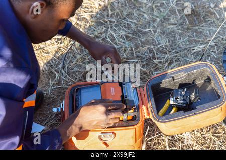 giunzione a fusione in fibra ottica, tecnico afroamericano che utilizza un hardware di giunzione portatile Foto Stock