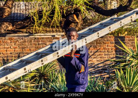 un tecnico africano porta una scala sulle spalle all'aperto Foto Stock