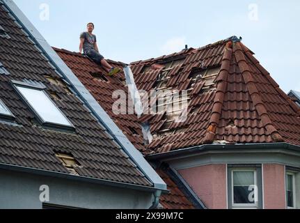 Hagen, Germania. 30 maggio 2024. Un conciatetto si siede su un tetto parzialmente coperto e attende che il raccoglitore di ciliegi gli fornisca nuove tegole. Dopo un forte vento - probabilmente un tornado - a Hagen, i lavori di pulizia sono proseguiti giovedì. Crediti: Bernd Thissen/dpa/Alamy Live News Foto Stock