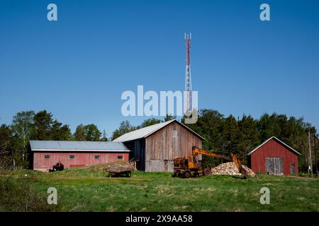 FARMYARD, LUMPARLAND, Åland: Vecchi fienili, capannoni di legno e macchine da scavo arrugginite in un'azienda agricola nel piccolo villaggio di Lumparby, nel Lumparland, il più piccolo distretto insulare principale di Åland, Mar Baltico, Finlandia. Foto: Rob Watkins. INFORMAZIONI: Lumparland è un comune delle Isole Åland, in Finlandia, noto per i suoi paesaggi panoramici e il patrimonio marittimo. Offre splendide coste, foreste lussureggianti e siti storici, tra cui la chiesa di Lumparland, rendendola una destinazione affascinante per gli amanti della natura e della storia. Foto Stock