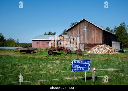 FARMYARD, LUMPARLAND, Åland: Vecchi fienili, capannoni di legno e macchine da scavo arrugginite in un'azienda agricola nel piccolo villaggio di Lumparby, nel Lumparland, il più piccolo distretto insulare principale di Åland, Mar Baltico, Finlandia. Foto: Rob Watkins. INFORMAZIONI: Lumparland è un comune delle Isole Åland, in Finlandia, noto per i suoi paesaggi panoramici e il patrimonio marittimo. Offre splendide coste, foreste lussureggianti e siti storici, tra cui la chiesa di Lumparland, rendendola una destinazione affascinante per gli amanti della natura e della storia. Foto Stock