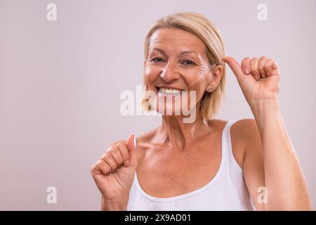 Ritratto di una bella donna matura che usa il filo interdentale. Foto Stock