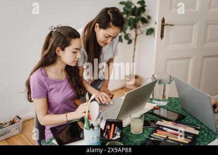 Madre che assiste la figlia mentre impara con il laptop sul tavolo a casa Foto Stock
