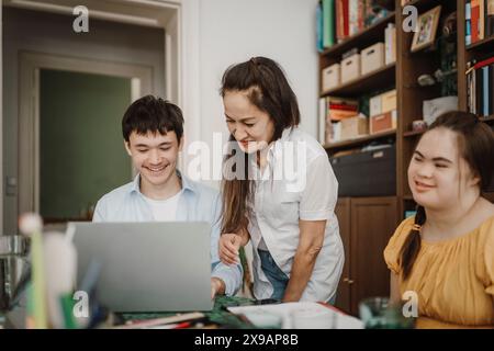 Donna sorridente che assiste il figlio e la figlia disabile mentre studia a casa Foto Stock