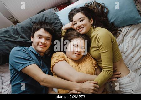 Direttamente sopra il ritratto dei fratelli che abbracciano la sorella della sindrome di Down mentre si sdraiano a letto a casa Foto Stock