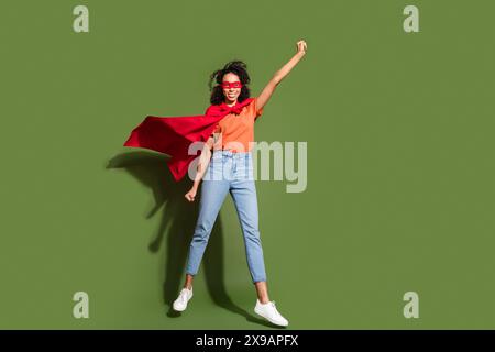 Foto a figura intera di una bella giovane donna che vola supereroina vestito elegante di arancio, isolata su sfondo color cachi Foto Stock