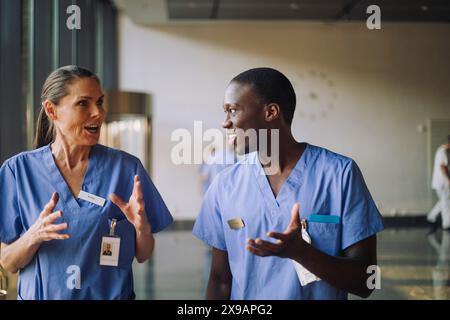 Medici maschili e femminili in scrub blu discutere mentre cammina in ospedale Foto Stock