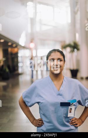 Ritratto di medico donna sicuro di sé in piedi con le braccia akimbo in ospedale Foto Stock
