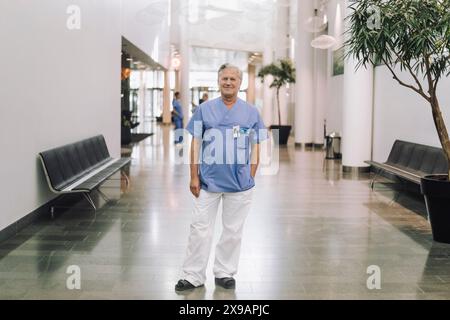 Ritratto a tutta lunghezza di sorridere medico anziano in piedi nella hall dell'ospedale Foto Stock