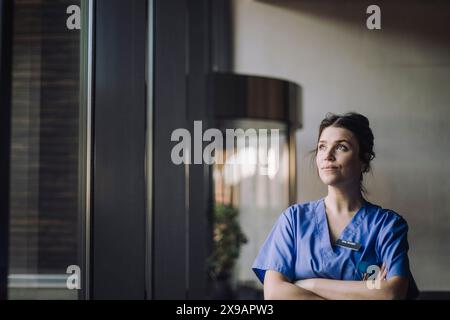 Medico donna premuroso in scrub blu in piedi con le braccia incrociate in ospedale Foto Stock