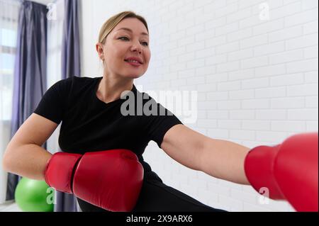 Un'atleta sorridente pugile che si allunga e riscalda il corpo prima di allenarsi di pugilato, indossa guanti da boxe rossi, allenati su wh Foto Stock