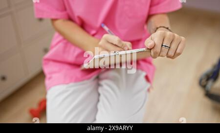 Primo piano di un professionista sanitario femminile in scrub rosa prendendo appunti in un interno di una clinica. Foto Stock