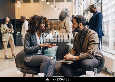 Donna d'affari che pianifica strategie con un imprenditore seduto sul divano al centro convegni Foto Stock