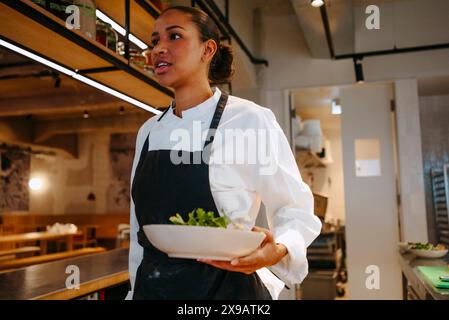 Chef donna che cammina con un'insalata nella cucina commerciale Foto Stock