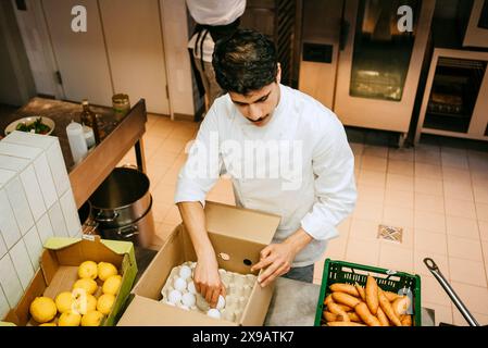 Vista ad angolo alto dello chef maschio che rimuove l'uovo dalla cassa mentre si trova in una cucina commerciale Foto Stock