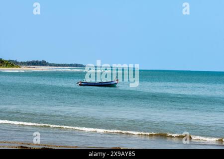 Una scena tranquilla si dispiega con una singola barca di legno che galleggia sulle calme acque blu di un mare esteso, sotto un cielo limpido. Foto Stock