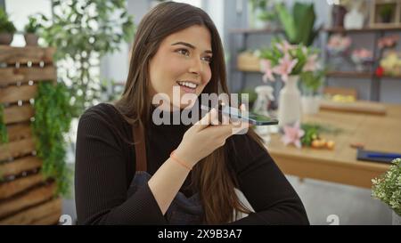 Una gioiosa donna ispanica che parla al telefono in un negozio di fiori, circondata da piante e fiori colorati. Foto Stock