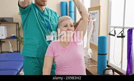 Un fisioterapista assiste una donna matura durante una sessione di riabilitazione in una sala terapeutica ben attrezzata. Foto Stock