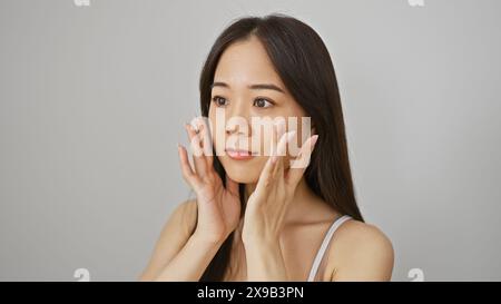 Una giovane donna cinese con una bellezza naturale posa su uno sfondo bianco isolato, toccando graziosamente il suo viso. Foto Stock