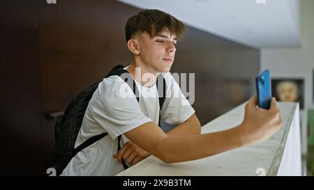 Adolescente caucasico scatta selfie con lo smartphone nella biblioteca universitaria Foto Stock