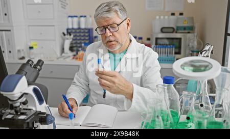 Un uomo scienziato maturo esamina una provetta in laboratorio, circondata da apparecchiature. Foto Stock